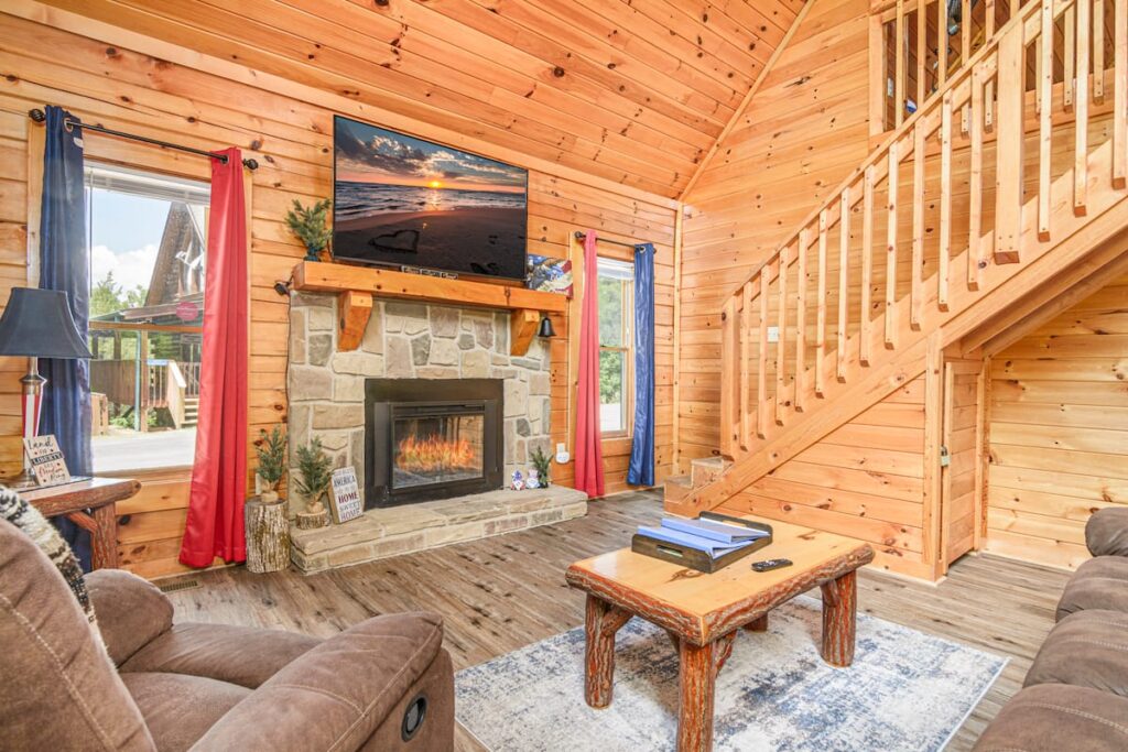 Wood-paneled living room with stone fireplace and stairs to the loft at American Way Cabin